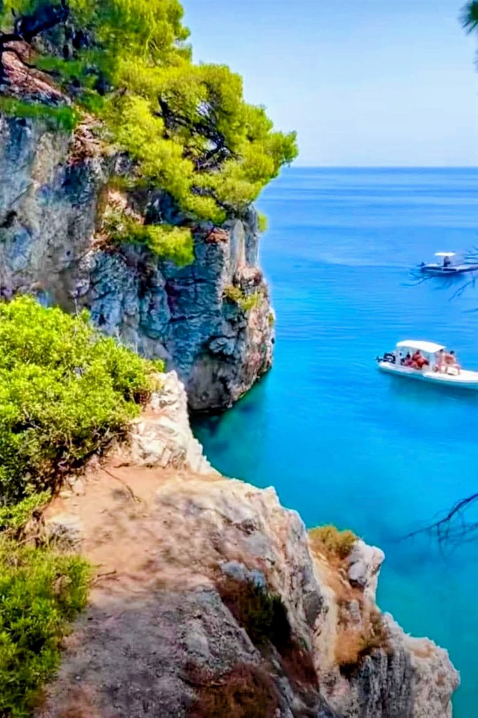 Pine-topped cliffs above a turquoise cove with boats