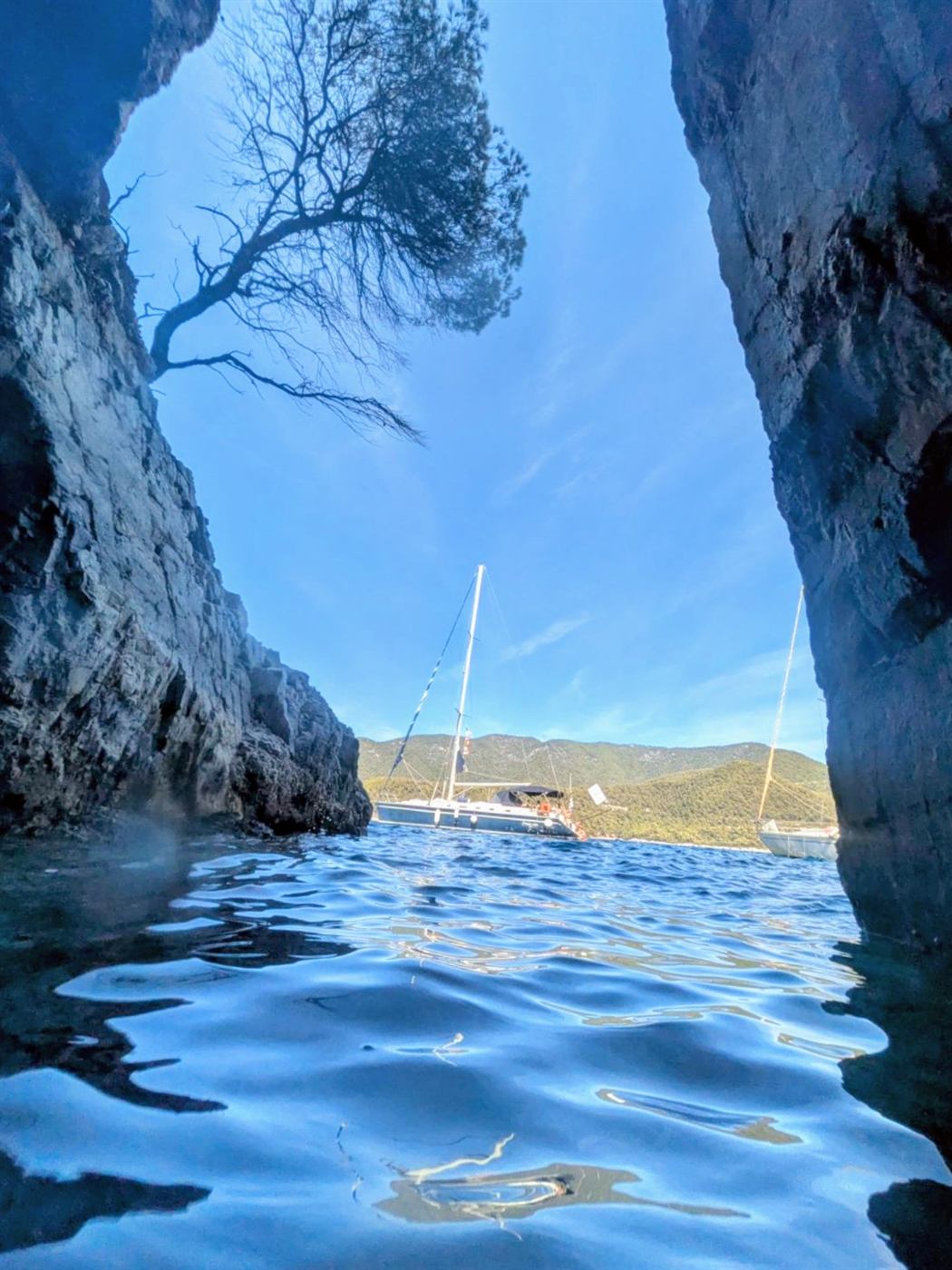 Sea cave opening onto a bay with a sailing yacht in the distance