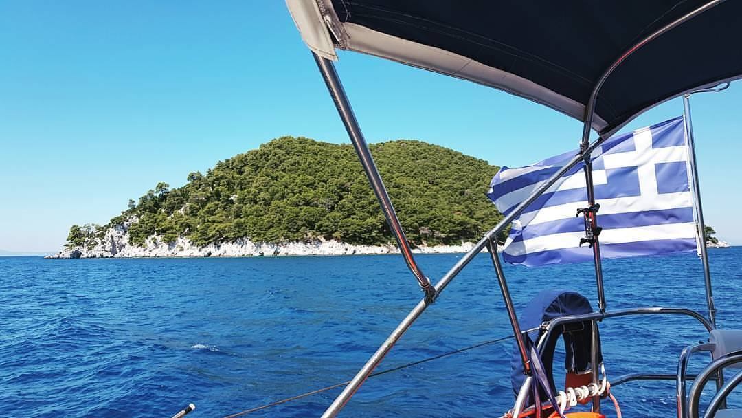 Greek flag flying at the stern with an island beyond