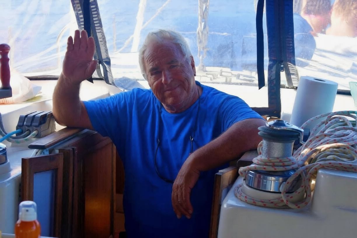 Captain Christos at the helm, raising a hand in welcome