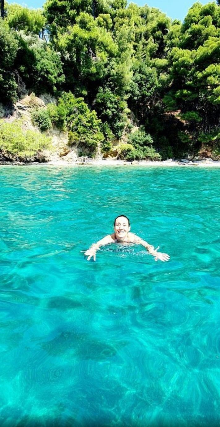 Swimmer floating in clear turquoise water beneath green pines